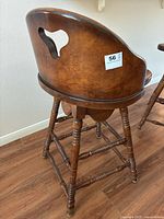Rear angle of the solid wood swivel bar stool showing the curved backrest with a cut-out handle and turned spindle legs and crossbars.
