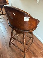 View of the back and side of the solid wood swivel bar stool showing the curved backrest, cutout, and turned legs.