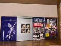 Four Beatles-related DVD cases displayed on a shelf: Concert for George, A Hard Day’s Night, The Ed Sullivan Shows, and The First U.S. Visit.