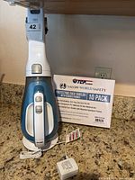 Black & Decker 16V mini vacuum placed on countertop with charger cord and a box of 10 TCP protective face shields