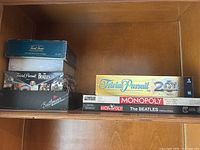 Photo showing stacked board games including Trivia Pursuit 20th Anniversary and Beatles editions of Monopoly and Trivia Pursuit