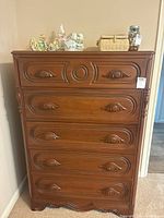 Front view showing entire chest of drawers with decorative carved drawer fronts and accessories on top.