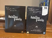 Two black DVD box sets of The Addams Family placed side by side, one labeled 'The Complete Series' and the other 'The Complete Seasons 1-3, 9 Disc Set, 63 Spooky Episodes'.