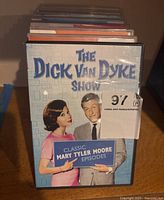 Front cover of The Dick Van Dyke Show DVD featuring Mary Tyler Moore and Dick Van Dyke with a sign reading 'Classic Mary Tyler Moore Episodes'.