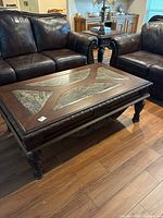 Coffee table positioned between two dark brown leather couches on wood floor, showing front and side view.