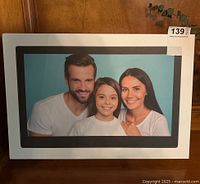 Front view of the new in box digital photo frame packaging showing a family photo on the device's display.