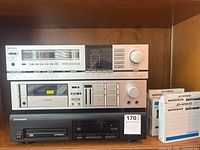Photo showing three stacked electronics: Hitachi silver AM-FM stereo tuner amplifier on top, Pioneer cassette deck in the middle, and Pioneer CD player below, plus three compact disc magazines on the right side.