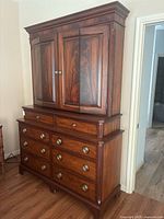 Front view of Ethan Allen solid wood entertainment center showing upper cabinet with paneled doors and lower chest of drawers with metal ring pulls.