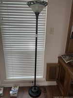 Full view of the tall fluted floor lamp with its frosted glass bowl-shaped shade and sturdy metal base next to a window with blinds.