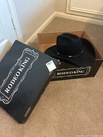 Black Rodeo King cowboy hat inside original black Rodeo King box on carpet floor.