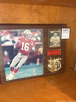 Wooden mounted plaque showing 8x10 photo of Joe Montana in red 49ers uniform (number 16), an NFL trading card, a Joe Montana nameplate, and a brass statue of football gear.