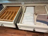 Photo showing kitchen towels folded neatly in drawer, including white, beige, and multi-color varieties.