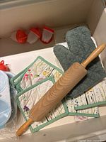 Top view of a wooden rolling pin, green kitchen mitt, plastic ice cream molds with red lids, and floral patterned kitchen towels.