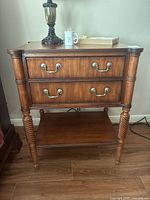 Front view of nightstand showing two drawers with brass handles, turned legs, and lower shelf.