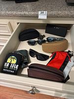 Opened drawer containing two pairs of Maui Jim sunglasses and one pair of Foster Grant sunglasses, along with several protective cases and a sunglasses holder pouch