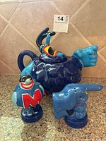 Blue character teapot with outstretched pointing hand and two ceramic salt and pepper shakers on tile countertop.