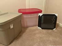 Three plastic totes, two Rubbermaid Roughneck Limited Edition beige totes and one clear tote with red lid, shown alongside one black picture frame with protective corners.