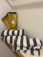 Four black and white striped beach towels rolled up and stacked on a wooden rail, next to one folded mustard yellow towel.