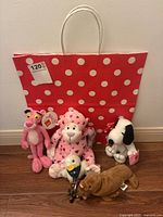 Wide shot showing all five stuffed animals arranged in front of polka dot gift bag on wooden floor.