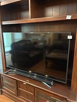 The full Samsung 59-inch TV placed inside a wooden cabinet, reflecting the room surroundings.