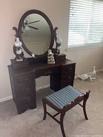 Photo front angle of antique solid wood vanity with oval mirror and upholstered bench