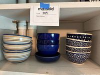Photo showing all 12 bowls stacked in three groups by design (striped, solid blue, and patterned) on a shelf.