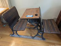 Antique school desk with wood top, wooden seat, and cast iron base in classic schoolhouse style.
