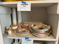 Photo of assorted floral porcelain dishware including cups, plates, bowls, creamer, and sugar bowl displayed on shelf and table.