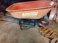 Orange metal wheelbarrow with a single wheel and black frame in garage setting