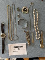 Full view of the assorted jewelry and watches laid out on blue fabric background, showing all necklaces, bracelets, pendants, brooches, and wristwatches