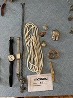 Photo showing assorted jewelry including necklaces, brooches, charms, and three watches with different styles and materials