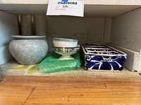 Shelf displaying five ceramic decorative items including a crackle glaze pot, two pedestal bowls, a blue and white planter and a small green wrapped item.