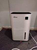 Front view of BRITSOU dehumidifier showing white body with water tank indicator window and power cord attached.