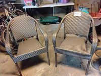 Two brown wicker patio chairs with metal frames placed side by side on a concrete floor.