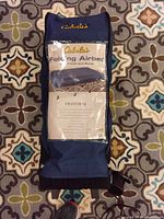 Blue Cabela's branded folding airbed stored in a zippered blue carrying bag placed on patterned carpet.