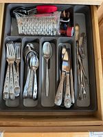 Drawer containing arranged stainless steel cutlery and kitchen tools, showing forks, spoons, knives, grater, and other utensils.