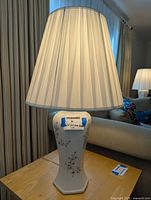 Front view of one white porcelain table lamp with floral design, pleated lampshade visible.