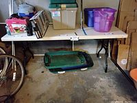 Image showing the plastic folding table in a garage or basement setting with various other items on and under the table.