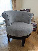 Front angle view of gray fabric upholstered contemporary accent chair showing curved back and wooden legs on hardwood floor.