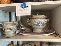 Soup tureen with lid, six stack cups, ladle, and large serving plate on shelf.