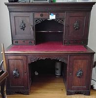 Front view of antique solid wood desk, showing carved wood panels and red leather writing surface.