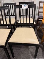 Front view of four black/dark brown wooden folding chairs with beige vinyl seats arranged together.