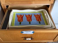 Three trays stacked inside a drawer: decorative tulip serving tray on top, other trays below.