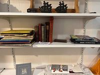 Shelf with vintage books and two cast metal ship figurines on top shelf.