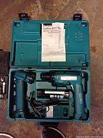 Makita cordless drill set inside teal case with battery, charger, and manual, showing drill and accessories neatly organized.