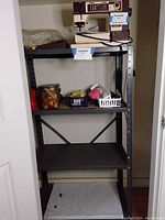 Full view of black metal shelving unit with three shelves, shelving located inside closet space, shows scale and configuration.
