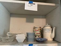 Shelf photo showing mixed dishware, candy dish, blue bowls, small rectangular white dishes, porcelain teapot, and multicolor cup.