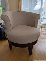 Side view showing beige fabric upholstery, wooden base, and legs with curved backrest and armrests.