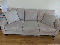 Beige fabric modern sofa with three seats and two beige cushions on light hardwood floor.
