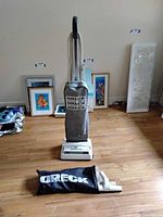 Oreck XL upright vacuum cleaner with bag and hand vacuum placed on hardwood floor with artwork in background